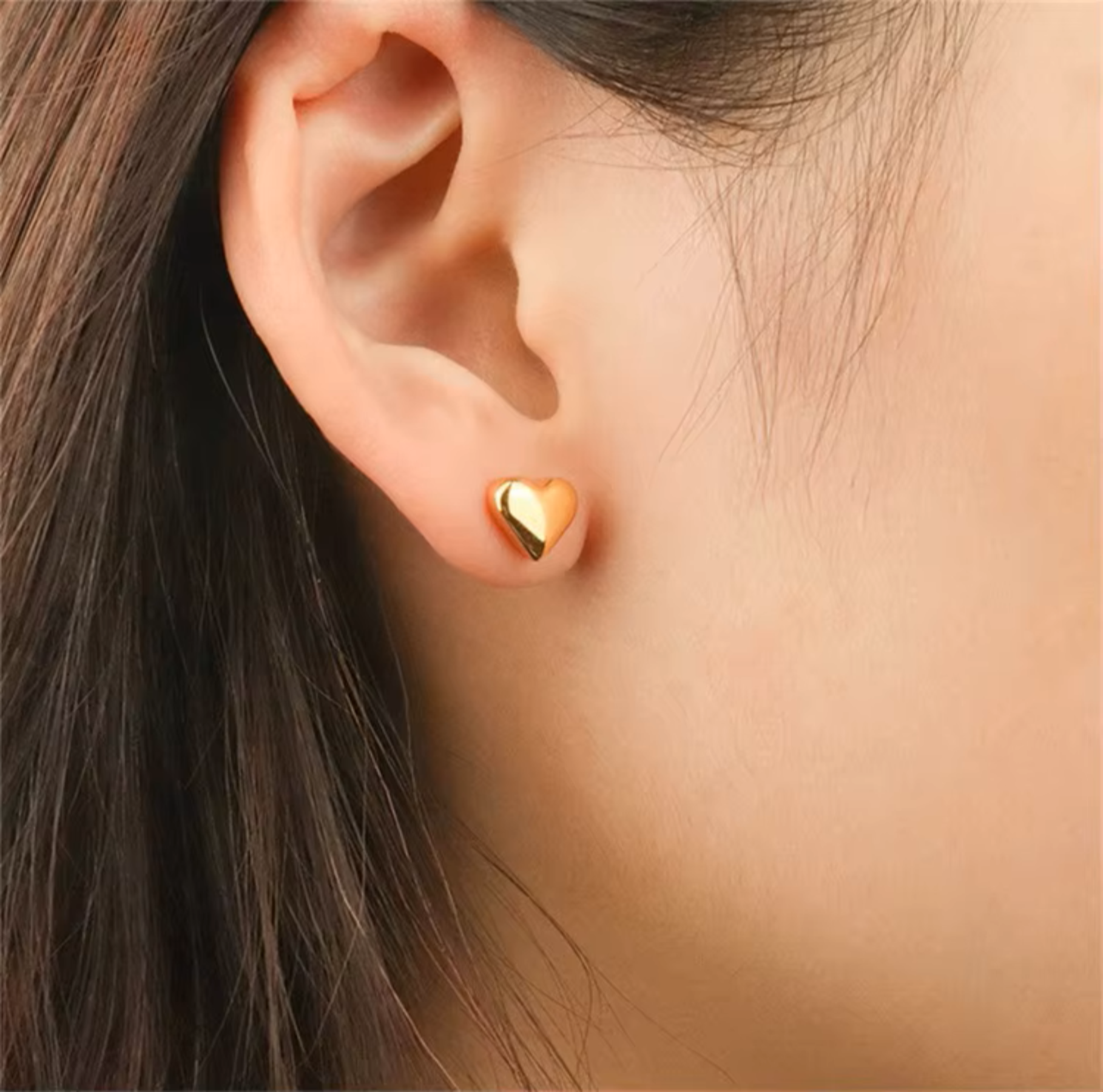 Close-up of an ear wearing a gold heart-shaped earring.