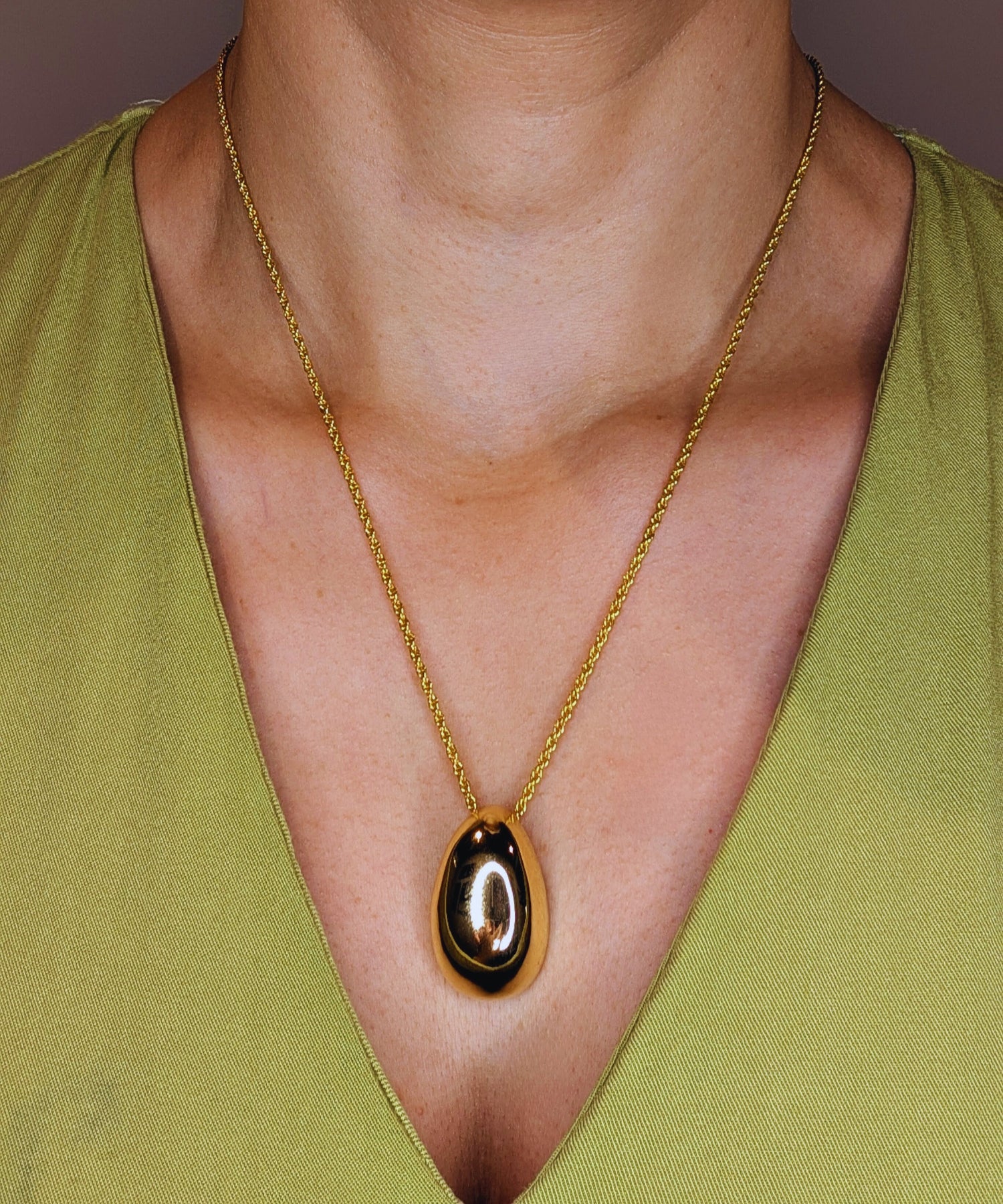 Gold necklace with a pendant on a person wearing a green top.