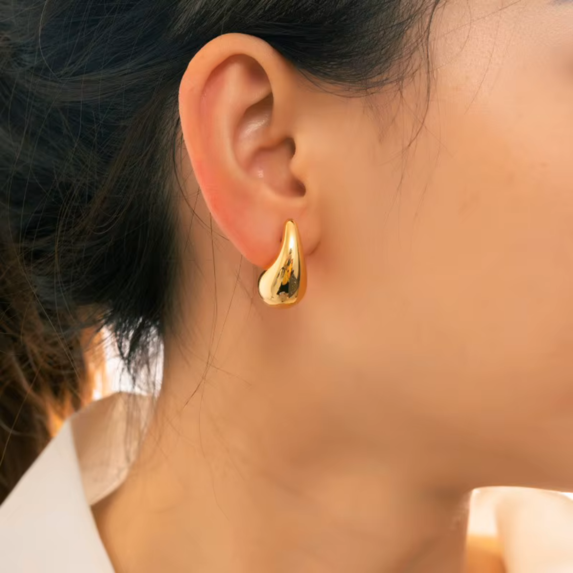 Gold earring worn by a person with blurred background
